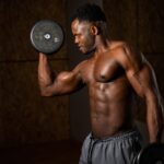 Shirtless athletic man curling free weights.