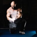 Shirtless bodybuilder applying chalk to his hands before lifting weights.
