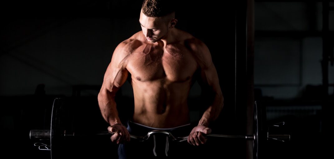 Bodybuilder curling a barbell in a dark gym.