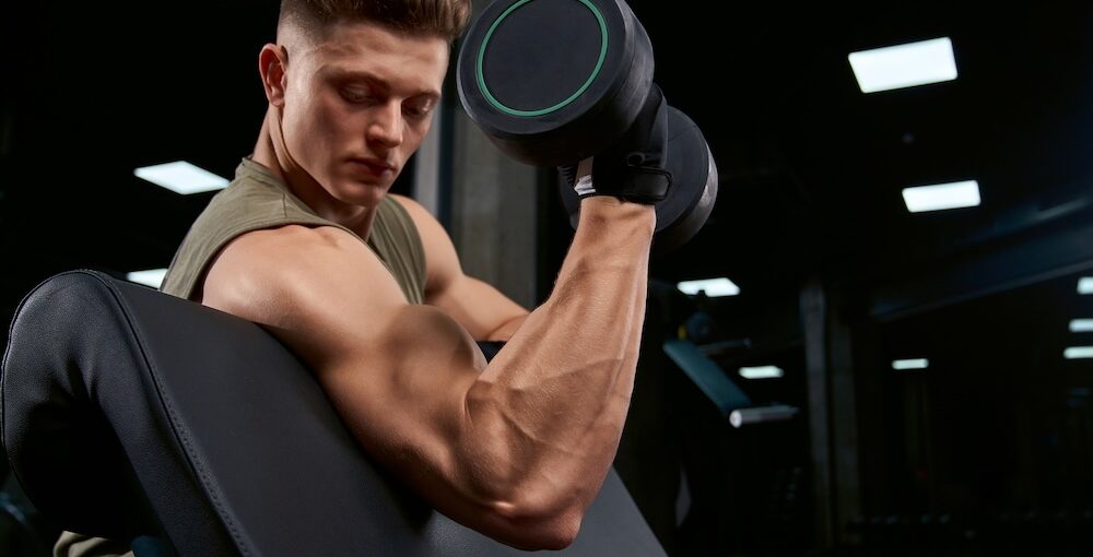 Bodybuilder training biceps with dumbbell on bench.