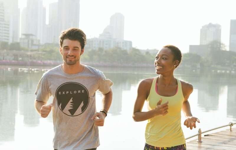 man and woman jogging alongside waterfront in city