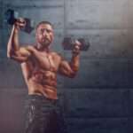 Strong man lifting weights in front of concrete wall