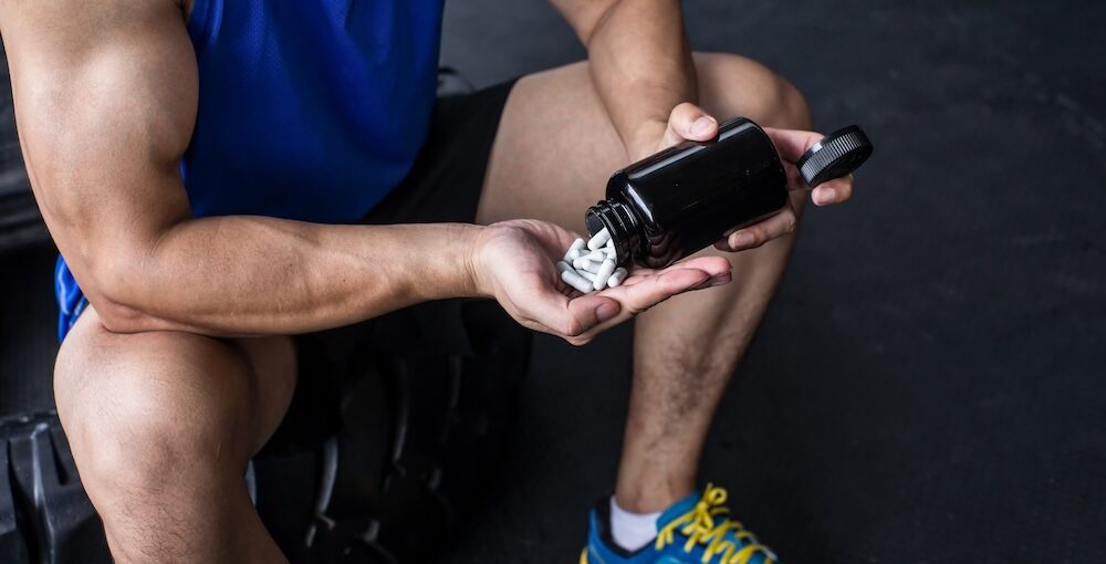 A man pouring prohormone pills into his hand at the gym