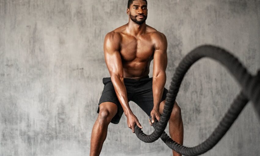 Man with no shirt on working out with battle ropes.