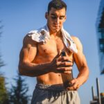 Man holding pre workout shake with shirt placed on shoulders outside