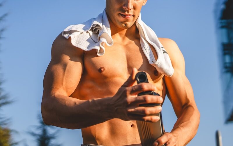 Man holding pre workout shake with shirt placed on shoulders outside