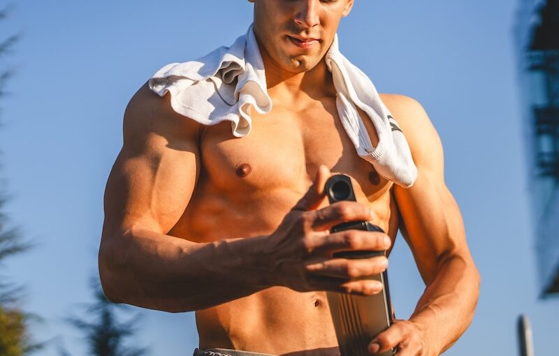 Man holding pre workout shake with shirt placed on shoulders outside