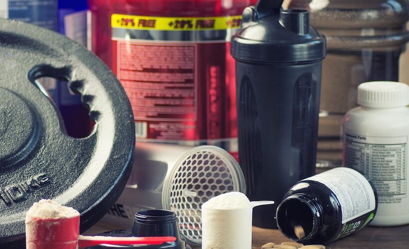 An assortment of bodybuilding supplements, containers, and a weight.