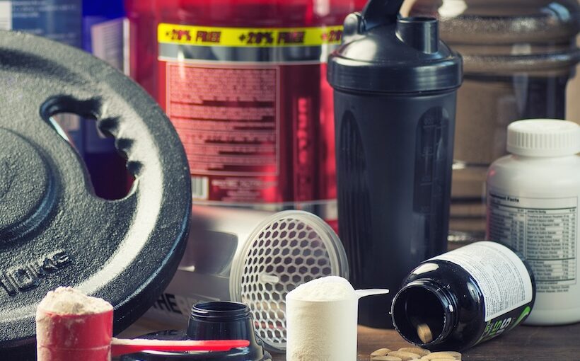 An assortment of bodybuilding supplements, containers, and a weight.