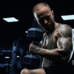 Side photo of tattooed weightlifter performing bicep curls with a dumbbell.