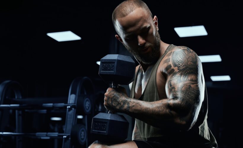 Side photo of tattooed weightlifter performing bicep curls with a dumbbell.